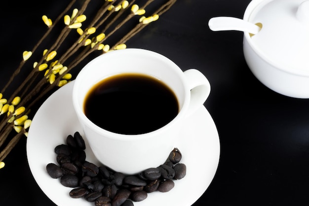 Internationale koffiedag traditionele Colombiaanse drank bovenaanzicht van mok koffie met gebrande koffiebonen en suikerpot op zwarte tafel versierd met bloemen