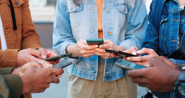 Internet addiction. Close up view of the company of multiracial people standing at the circle and being deep at their gadgets while spending time at the internet