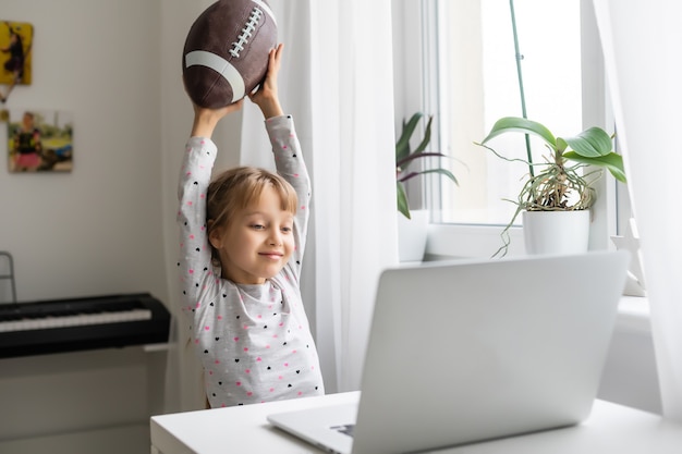 Internet addiction and computers concept with kid and laptop, little girl with rugby ball