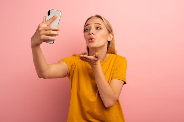 Photo internet connected blonde cute girl sends hearts on her smartphone