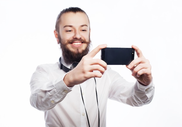 Internet technologie en mensen concept een jonge man met een baard in hemd met een mobiele telefoon en een foto van zichzelf terwijl hij tegen een witte achtergrond staat