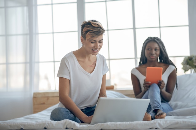 On internet. Two girls sitting on the bed and spending time on internet