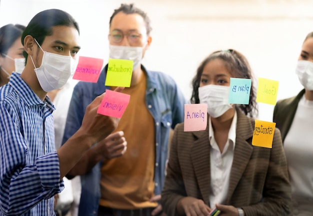 Foto interraciaal aziatisch business team brainstormidee op kantoorvergaderruimte na heropening vanwege coronavirus covid-19 stadsvergrendeling. ze dragen een gezichtsmasker om het risico op infectie te verminderen als een nieuwe normale levensstijl.