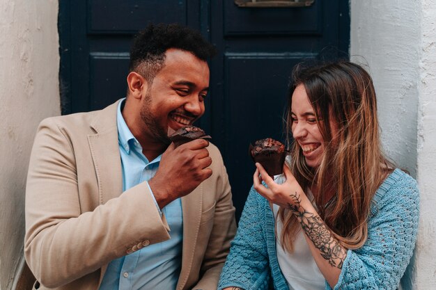 Interracial couple of an African American boy and a Caucasian girl sitting in a doorway while eating a chocolate cupcake