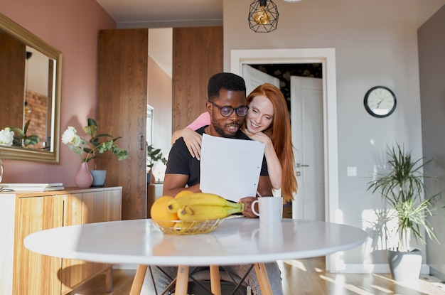 Interracial couple reading mail and checking accounting in the kitchen at home