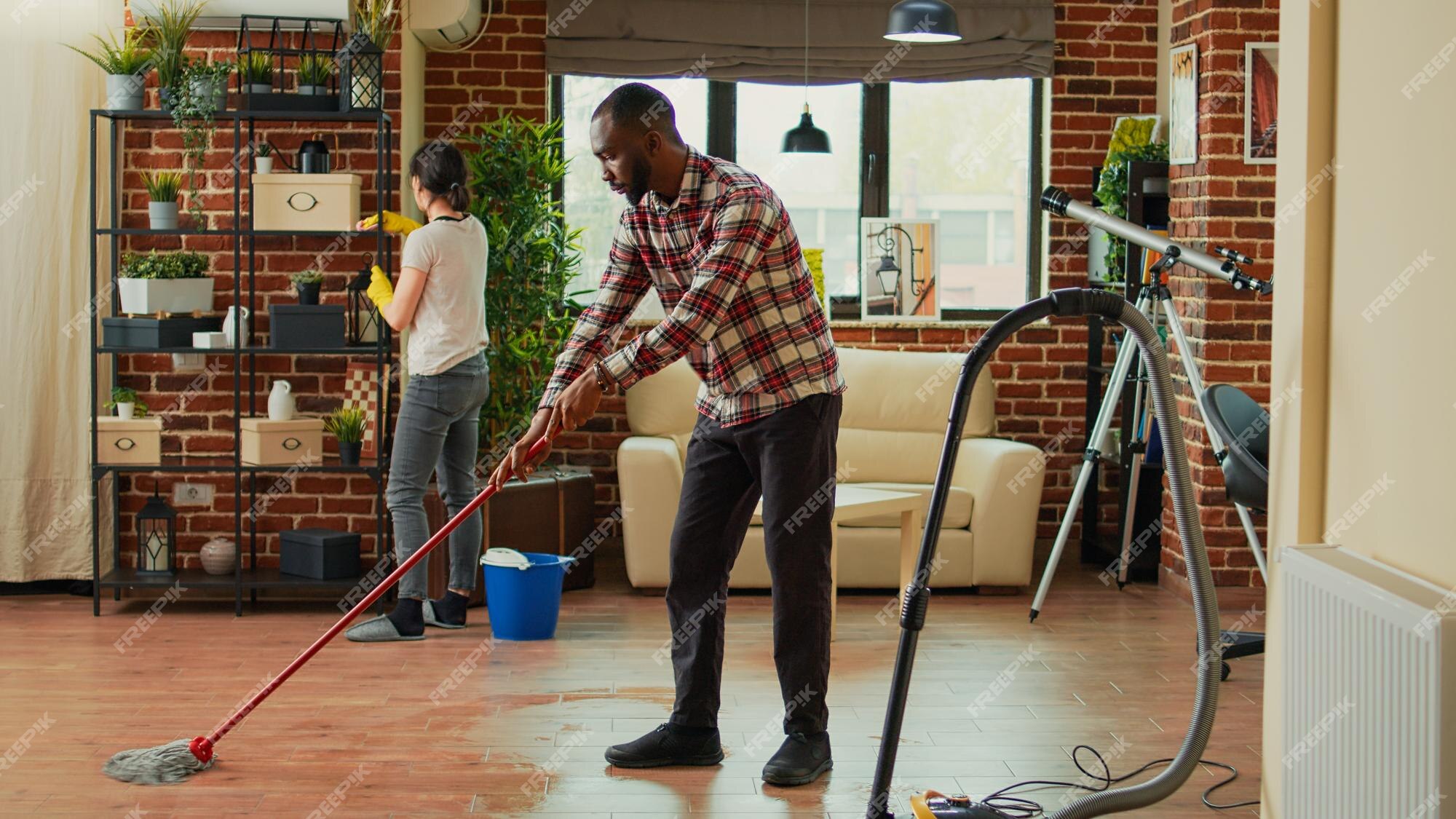 Close up of African American young female and male professional cleaners  vacuuming floor with vacuum in modern room, cleaning service, small  business, working in apron, clean house concept Stock Photo