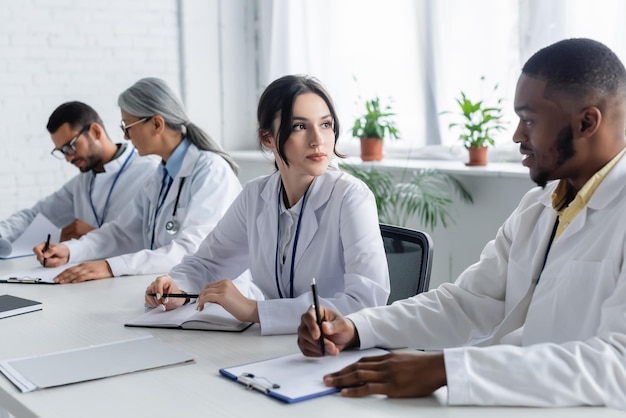 Photo interracial doctors looking at each other near blurred colleagues