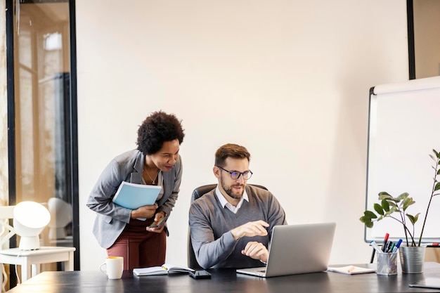 An interracial mentor is standing next to a mentee at the office and giving him advices