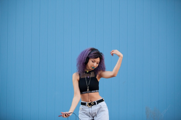 Interracial teenager dancing to the music on a blue wall