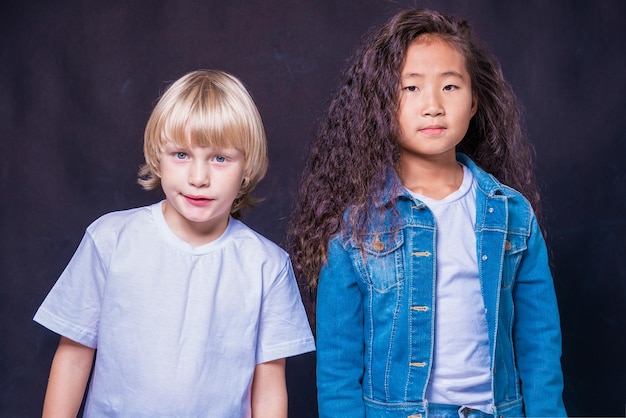 Foto interraciale kinderen twee kinderen van blanke en aziatische blonde jongen en brunette meisje op een blauwe achtergrond in de studio concept vriendschap van volkeren