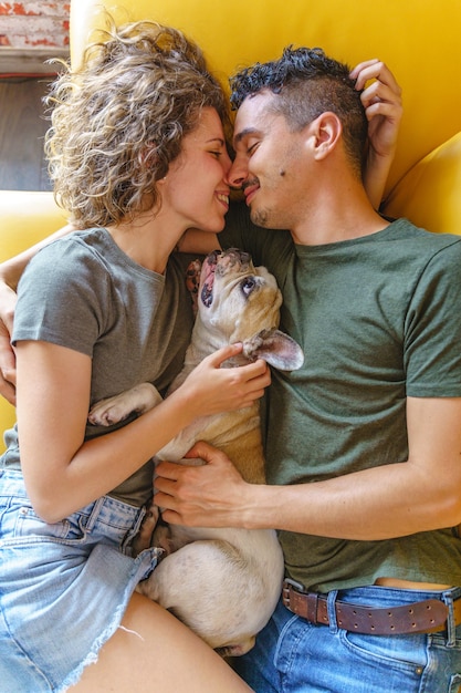 Foto intiem moment van paar zoenen met hond thuis. verticaal bovenaanzicht spelen met huisdier op de bank.