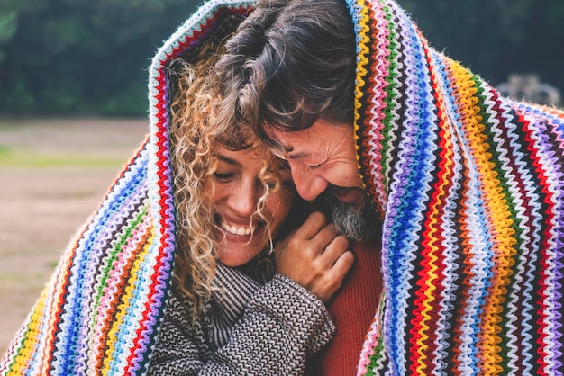 Foto momenti intimi, divertenti e felici con una coppia adulta in attività di svago all'aperto coperti da una copertina colorata a maglia al parco un uomo e una donna in amore e in relazione insieme al parco