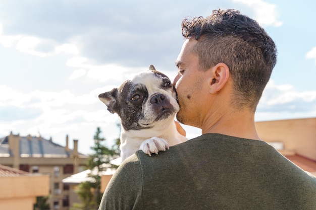 認識できない男が屋外で犬にキスする親密な瞬間。彼の犬を愛する男の水平側面図。