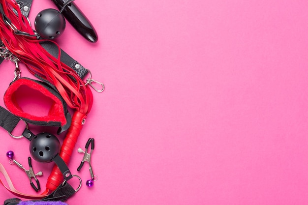 Photo intimate sex games. bdsm tools dildo vibrator, gag, nipple clamps, handcuffs, whip and other on red pink background. free space for your text.