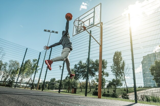 Into the basket. Low angle of a nice young man jumping up while throwing the ball in the basket