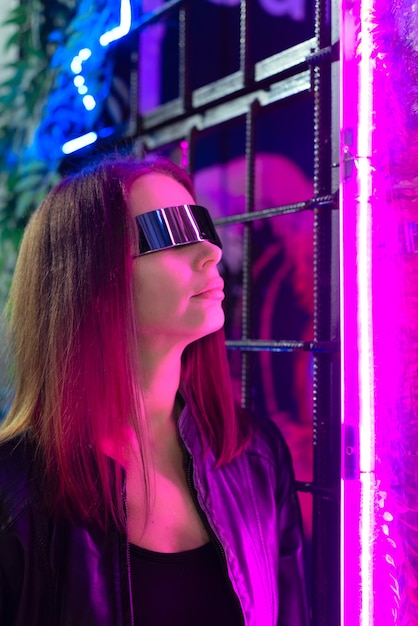 Intreepupil mooie jonge vrouw in kosmische bril die 's nachts naast kleurrijk neonlicht staat met selectieve focus Party disco neon nightclub vibes