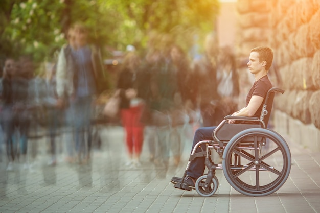 The invalid man sit in the wheel chair in the crowd stream at the pavement