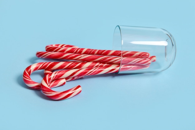 새해 크리스마스 캐러멜 사탕, 줄무늬 사탕 지팡이, 막대 사탕과 함께 파란색 배경에 누워 있는 거꾸로 된 유리. 웹 배너에 광고를 위한 크리스마스 장식