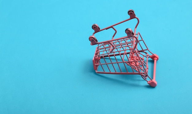 Inverted Mini pink supermarket trolley on blue background Shopping concept