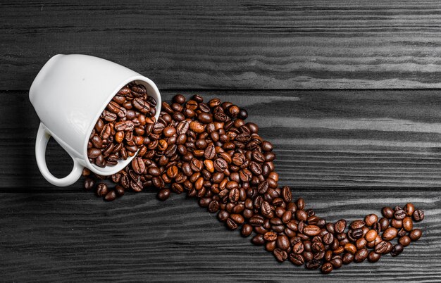 Inverted white cup with scattered coffee beans beautifully lying on the wooden surface. 