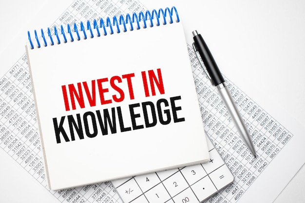 Invest In Knowledge inscription in a white notebook on the table next to a calculator, pen, numbers on a sheet of paper. Tax concept