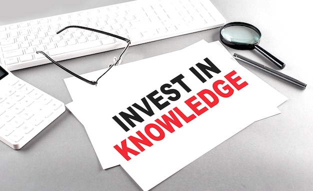 INVEST IN KNOWLEDGE text on a paper on a gray background near a calculator and a white keyboard