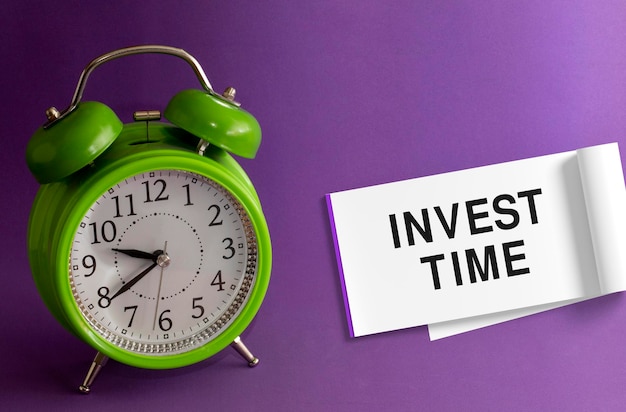 INVEST TIME in an office on a notepad purple background with a green table clock