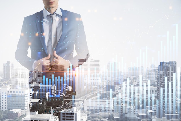 Investing and business analytics concept with digital financial screen with graphs and candlestick on city background with businessman double exposure