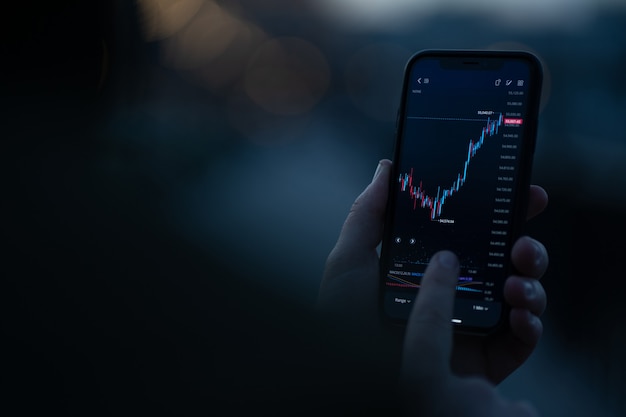 Photo investing online. male hand monitoring stock exchange data on smartphone, using investment app for analyzing price activity in real time. selective focus on mobile phone with financial chart on screen