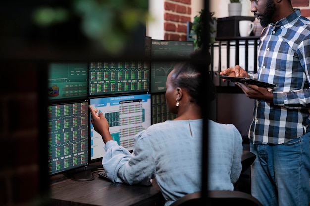 Investment company employees sitting at multi monitor workstation while analyzing real time trend charts. Forex stock market traders talking about capital budget and statistics charts.