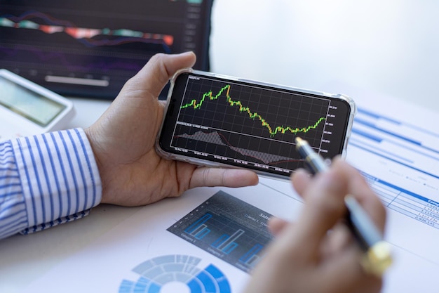 投資家は携帯電話やタブレットで株価チャートを見ています。彼は株式投資家です。彼はチャートを分析し、指標を使用して取引を開始することで株式を取引します。株式投資のアイデア。