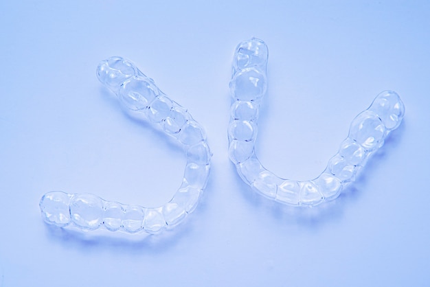 Invisible dental teeth brackets tooth aligners on blue background. Plastic braces dentistry retainers to straighten teeth.