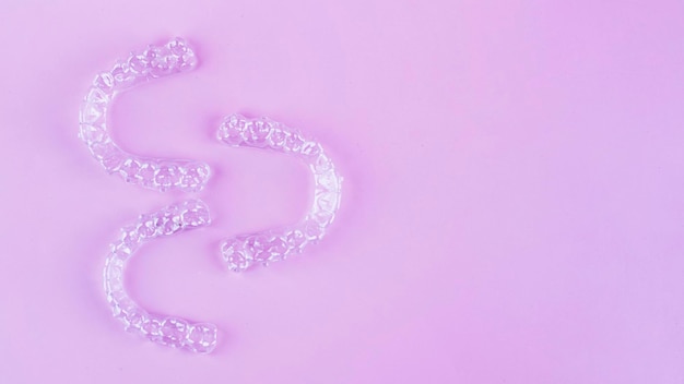 Невидимые зубные скобки зубные выравниватели на розовом фоне Пластиковые скобки