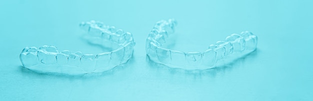 Invisible dental teeth brackets tooth aligners on turquoise background. Plastic braces dentistry retainers to straighten teeth.