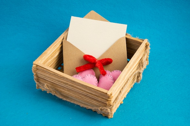 Invitation envelope in wooden wicker basket decorated with pink hearts isolated on blue