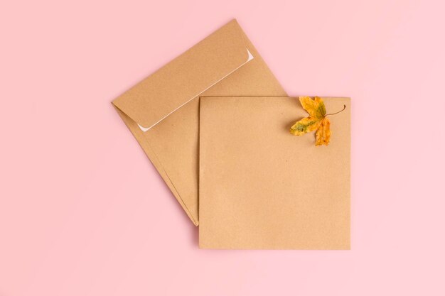 Invitation or greeting card mockup with craft envelopes on soft pink background with autumn leaf