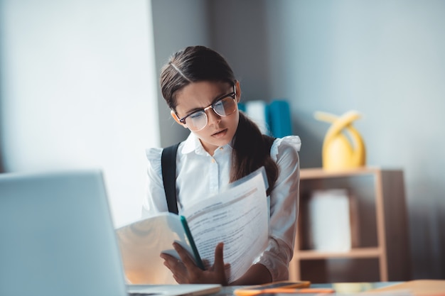 Involved. Brunette girl in eyeglasses reading a report and looking involved