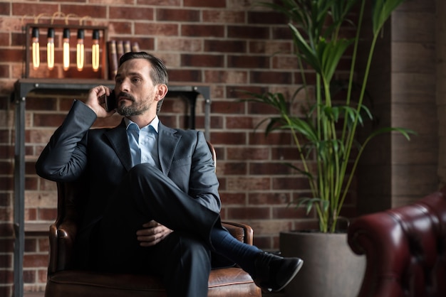 Involved in the discussion. Good looking attractive confident man sitting in an armchair and listening attentively to his interlocutor while having a conversation