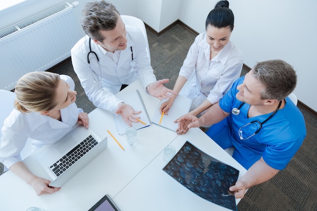 Oncologi competenti energici coinvolti che lavorano presso l'armadietto degli esami ed esaminano la foto del mrt mentre discutono e usano i gadget