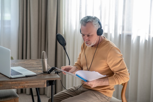 Involved. A gray-haired man in black headphones speaking in microphone and looking interetsed