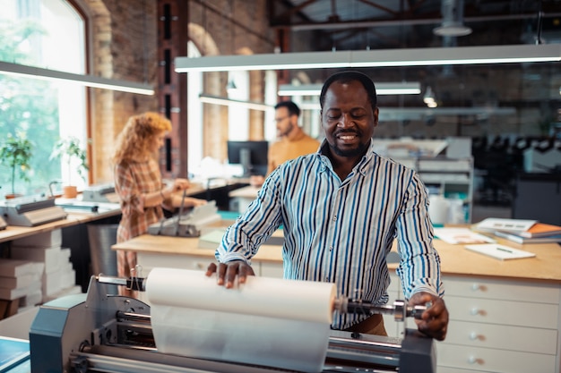 Involved in printing. Dark-skinned bearded man feeling involved in printing posters in the office