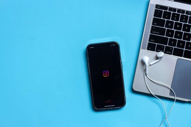 iPhone met Instagram-app-logo op het scherm met oortelefoons en toetsenbordlaptop geïsoleerd op blauwe bac