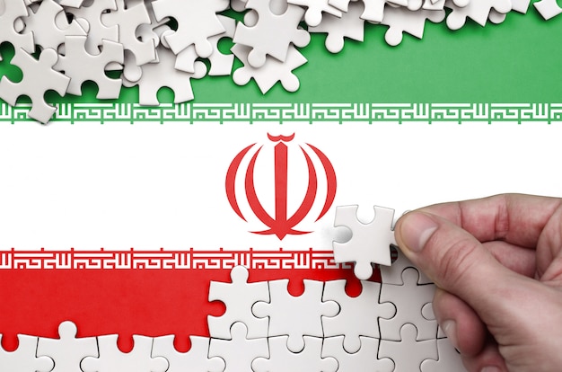 La bandiera dell'iran è raffigurata su un tavolo su cui la mano umana piega un puzzle di colore bianco