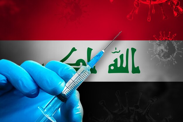 Iraq Covid19 Vaccination Campaign Hand in a blue rubber glove holds syringe in front of flag