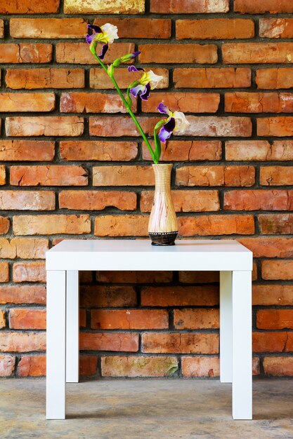 An iris flower in a vase on a white table against a brick wall background