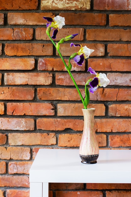 Irisbloem in een vaas op een witte tafel tegen een achtergrond van een bakstenen muurclose-up