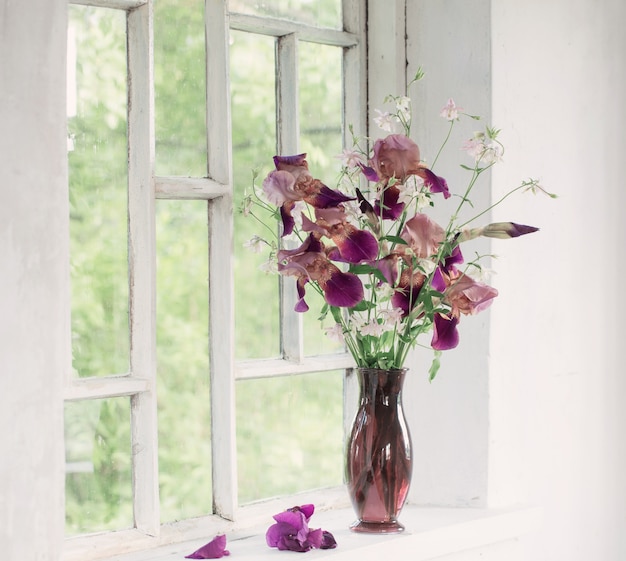 Irisbloemen in glasvaas op witte oude vensterbank