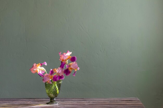 Irises in beautiful glass vase against green wall