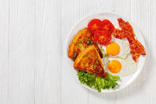 Photo irish breakfast of mashed potato cakes fried eggs bacon slices grilled tomatoes and fresh lettuce on white plate on white wooden table horizontal view from above flat lay free space