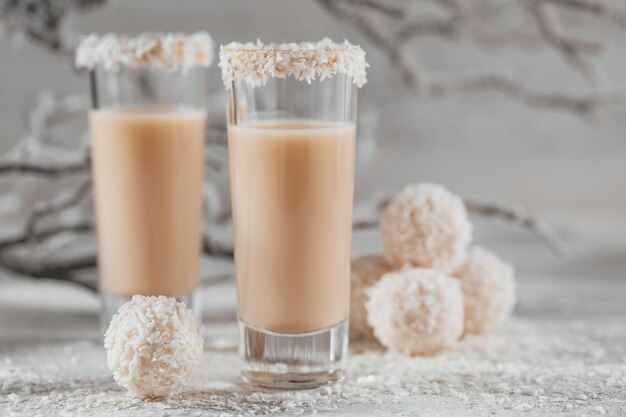 Irish cream or Coffee Liqueur with homemade coconut healthy balls and coco flakes on light background